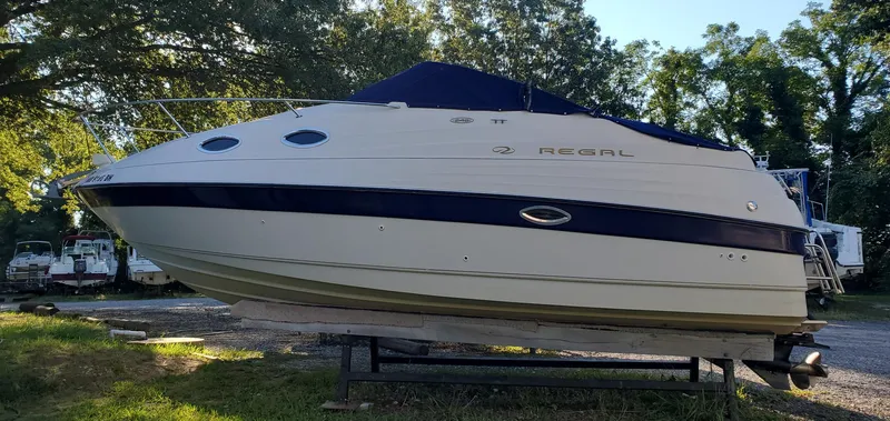 The Image of 1999 Regal Commodore 242 boat on trailer, parked outdoors with trees in the background. - 0