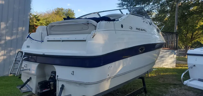 Slide: The Image of 1999 Regal Commodore 242 boat on display, white with blue accents, parked outdoors. - 2