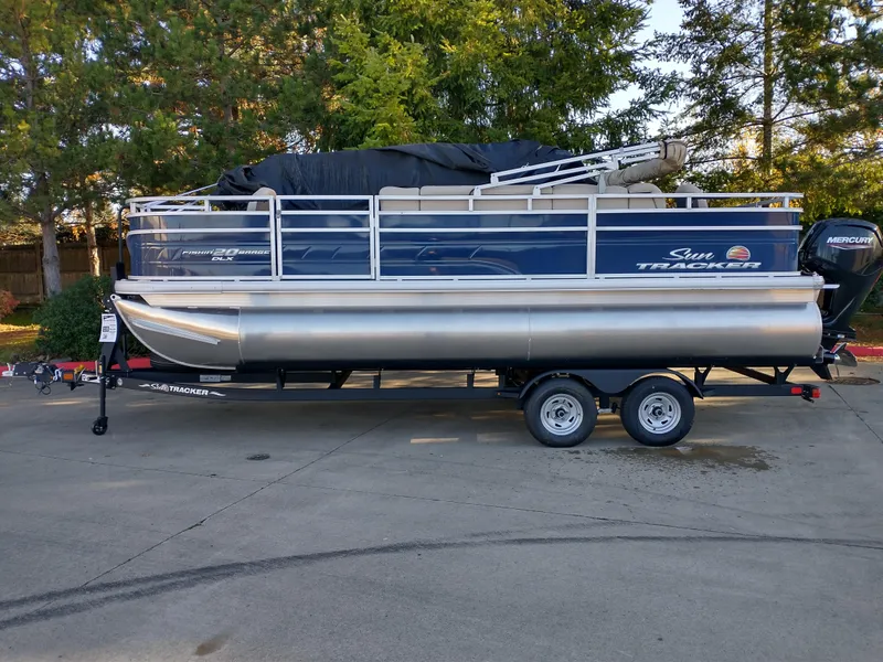 The Image of 2025 Sun Tracker Fishin' Barge 20 DLX pontoon boat on trailer, parked outdoors. - 0