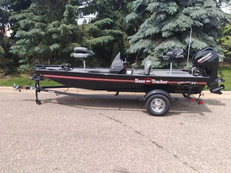 Slide: The Image of 2025 Tracker Bass Tracker Classic XL boat on trailer, parked on road with trees in background. - 5