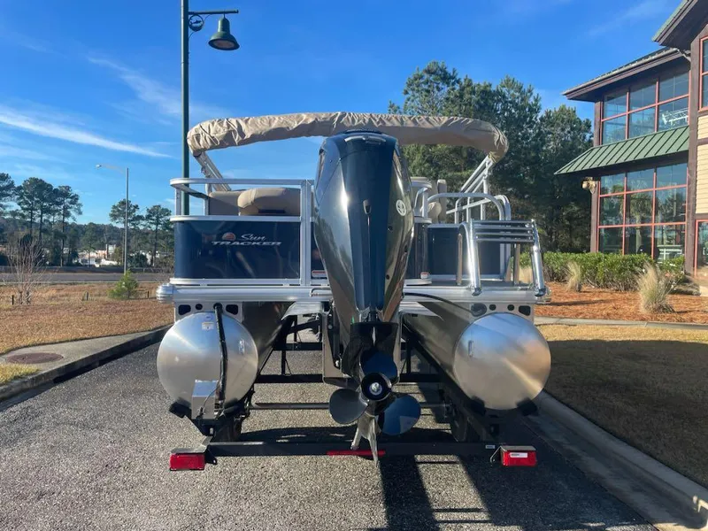 Slide: The Image of 2025 Sun Tracker Bass Buggy 18 DLX pontoon boat parked outdoors on a sunny day. - 2