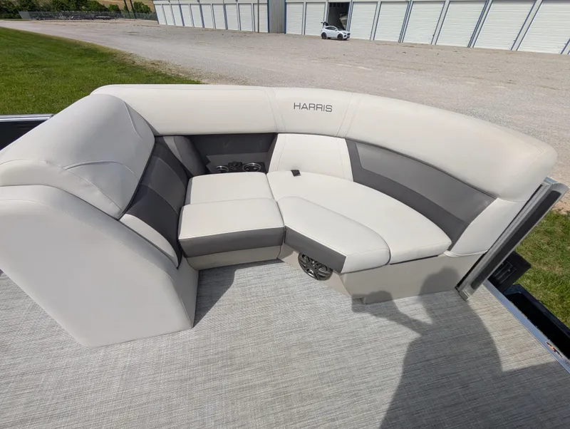 Slide: The Image of 2022 Harris Cruiser 210 boat with beige and gray seating, docked near storage units. - 10