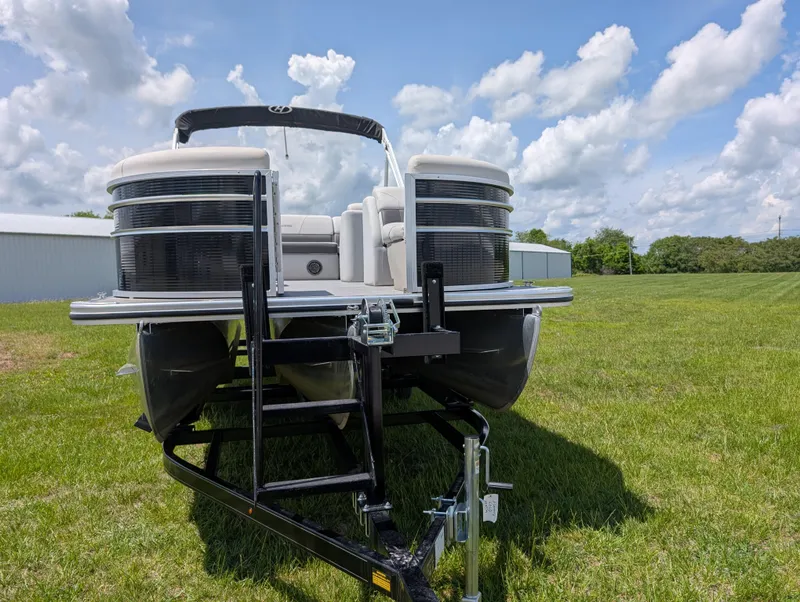 Slide: The Image of 2022 Harris Cruiser 210 pontoon boat on trailer, parked on grassy field under blue sky. - 2
