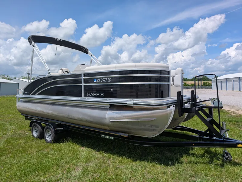 Slide: The Image of 2022 Harris Cruiser 210 pontoon boat on trailer, parked on grass under a cloudy sky. - 3