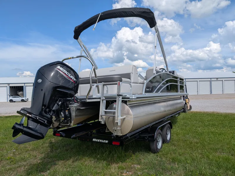 Slide: The Image of 2022 Harris Cruiser 210 pontoon boat on trailer, parked on grass under a blue sky. - 4