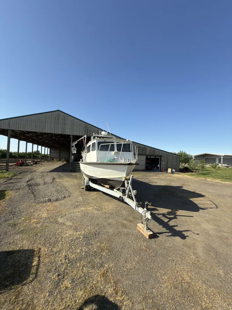Slide: The Image of 1975 Monark 30 Fishing Boat on trailer, parked outside a large shed under clear blue sky. - 27