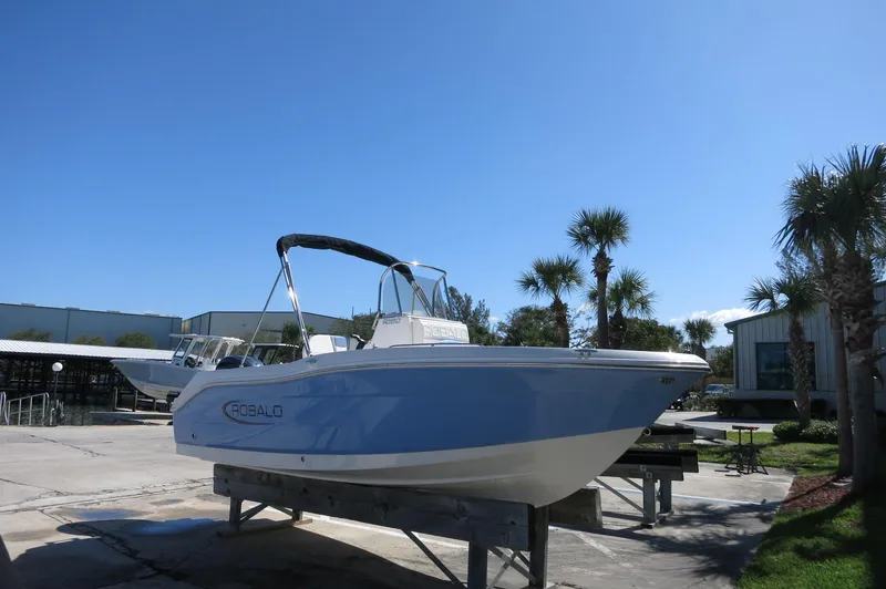 Slide: The Image of 2025 Robalo R180 Center Console boat on display outdoors, surrounded by palm trees. - 14