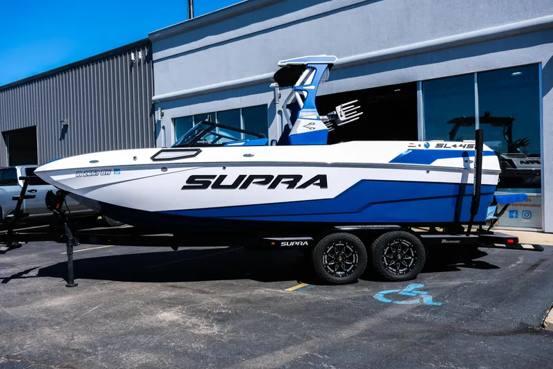 Slide: The Image of 2023 Supra SL boat on trailer, parked outside a building, showcasing sleek design and branding. - 2