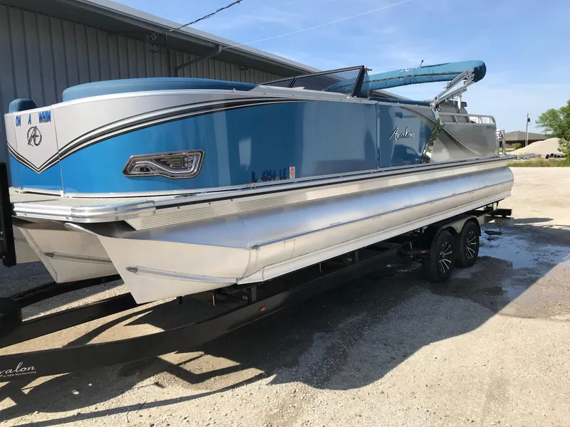 Slide: The Image of 2023 Avalon LSZ Elite Windshield pontoon boat in blue, parked on a trailer. - 1