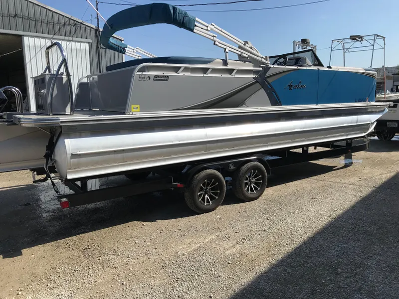 Slide: The Image of 2023 Avalon LSZ Elite Windshield pontoon boat on trailer, parked outdoors. - 12