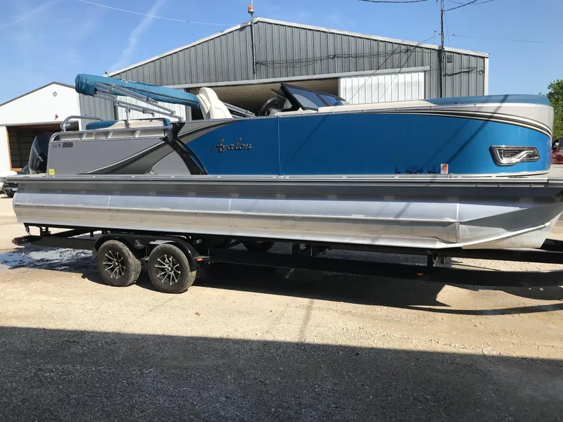 Slide: The Image of 2023 Avalon LSZ Elite Windshield pontoon boat on trailer, parked outdoors. - 13