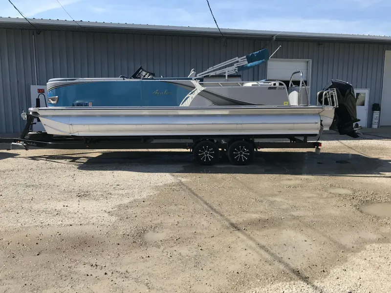 Slide: The Image of 2023 Avalon LSZ Elite Windshield pontoon boat on trailer, parked outdoors. - 2