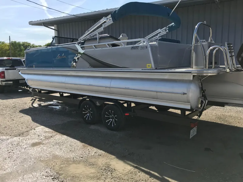 Slide: The Image of 2023 Avalon LSZ Elite Windshield pontoon boat on trailer, parked outdoors. - 3