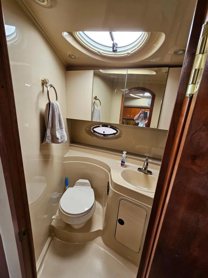 Slide: The Image of 2004 Cruisers Yachts 340 Express bathroom with toilet, sink, mirror, and porthole window. - 32