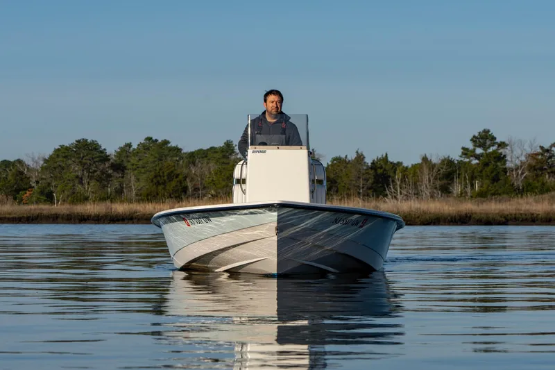 Slide: The Image of Man steering 2005 Pathfinder 2000v boat on calm water, with trees in the background. - 2