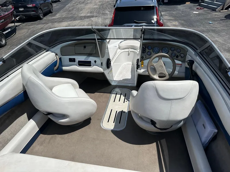 Slide: The Image of 2002 Crownline 180 BR boat interior with white seats and dashboard, parked outdoors. - 6