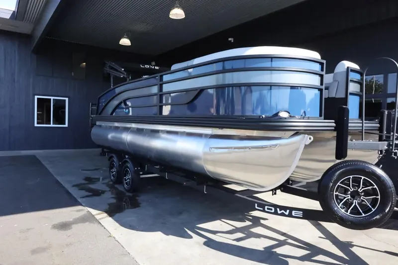 Slide: The Image of 2025 Lowe SS 210 DL pontoon boat on trailer, parked outside a building. - 2