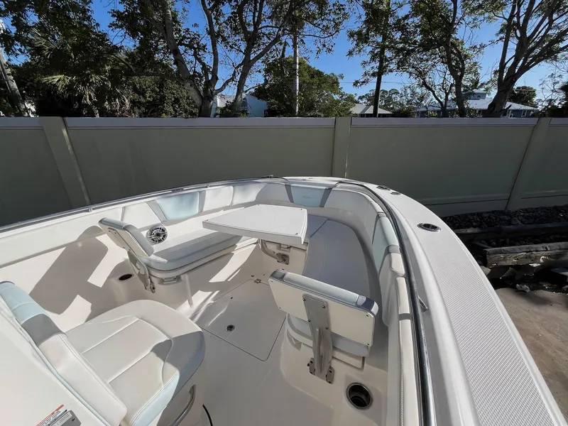 Slide: The Image of 2021 Robalo R272 Center Console boat interior with seating and table, surrounded by trees. - 6