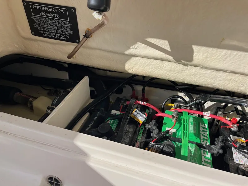 Slide: The Image of 2021 Robalo R272 Center Console boat battery compartment with wiring and discharge warning sign. - 9