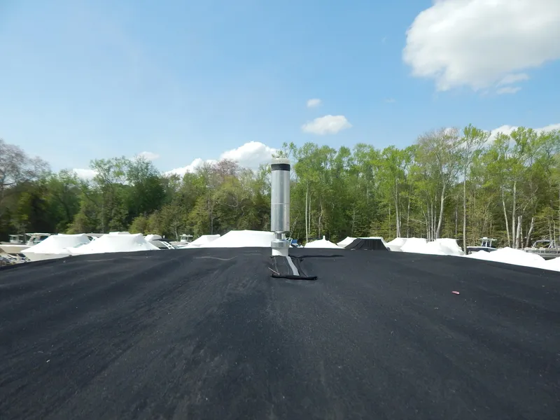 Slide: The Image of A black asphalt roof with a chimney vent, surrounded by trees under a blue sky. - 14