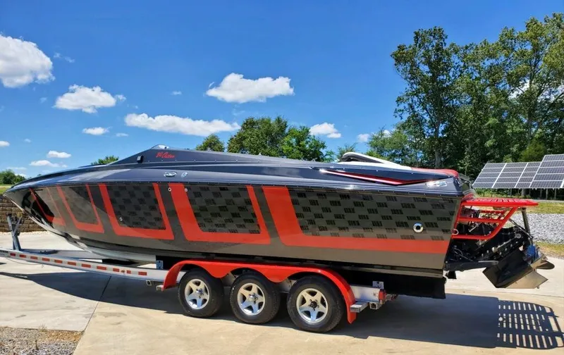 The Image of 2006 Baja Outlaw boat on trailer, black and red design, sunny day, blue sky background. - 0