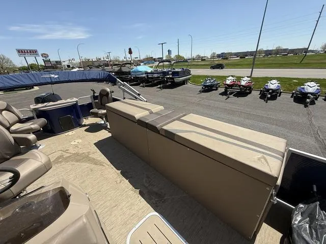 Slide: The Image of 2022 Bennington 23 SFXAPG pontoon boat interior with seating, parked near jet skis and dealership. - 26