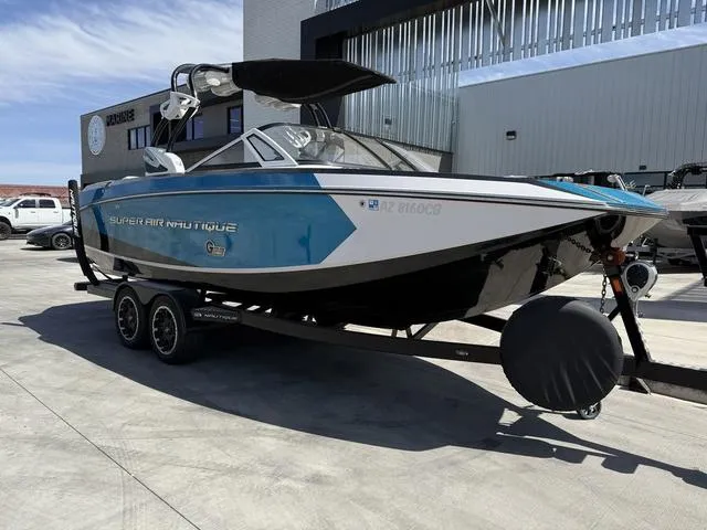 Slide: The Image of 2013 Nautique G23 boat on trailer, blue and white, parked outdoors. - 2