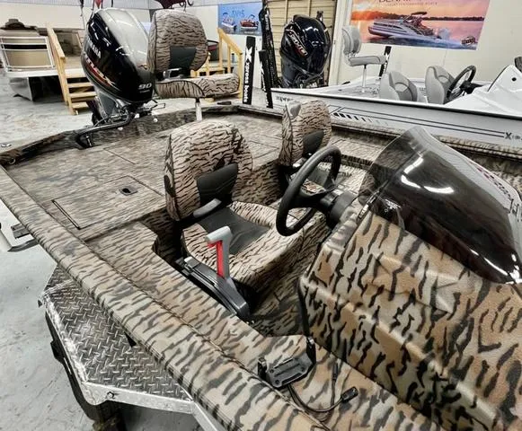 Slide: The Image of 2025 Xpress Boats XP180 with camouflage interior, steering wheel, and outboard motor in showroom. - 4