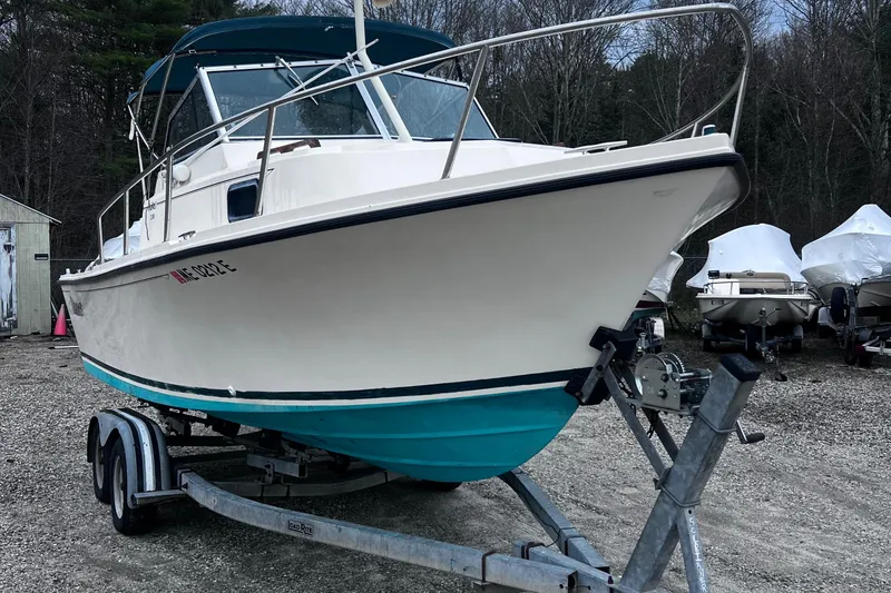 Slide: The Image of 1999 Parker 21 Cuddy Cabin boat on trailer, white hull with teal bottom, parked outdoors. - 1