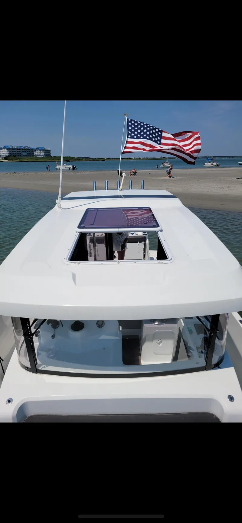 Slide: The Image of 2020 Beneteau Barracuda 8 boat with American flag, docked on a sunny beach. - 8