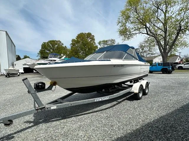 Slide: The Image of 2002 Bayliner 2150 boat on trailer, parked outdoors, with blue canopy and trees in background. - 1