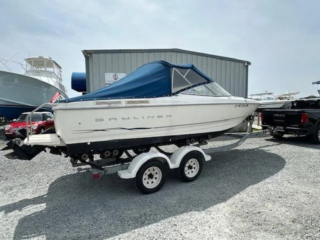 Slide: The Image of 2002 Bayliner 2150 boat on trailer, blue canopy, parked outdoors near a building. - 2