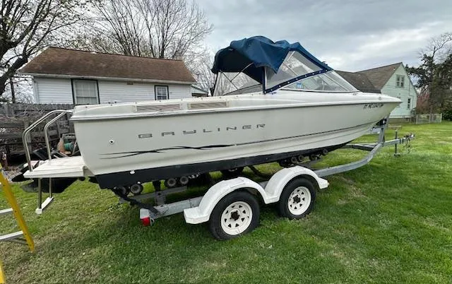 Slide: The Image of 2002 Bayliner 2150 boat on trailer, parked on grass near houses, under cloudy sky. - 3