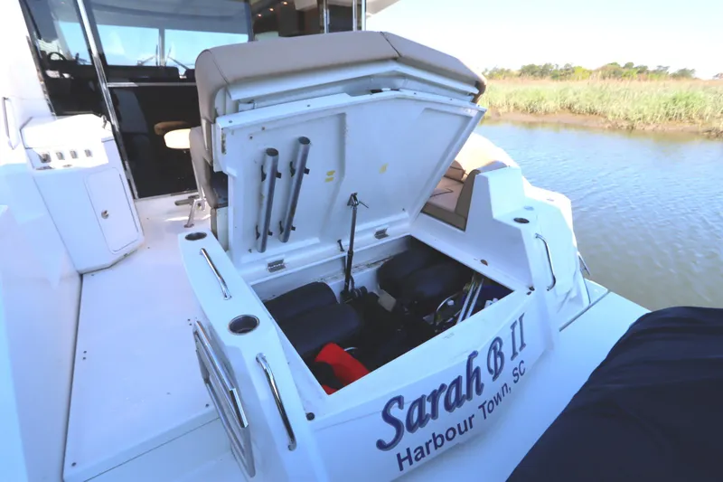 Slide: The Image of 2015 Cruisers Cantius boat with open storage compartment, docked near grassy shoreline. - 14