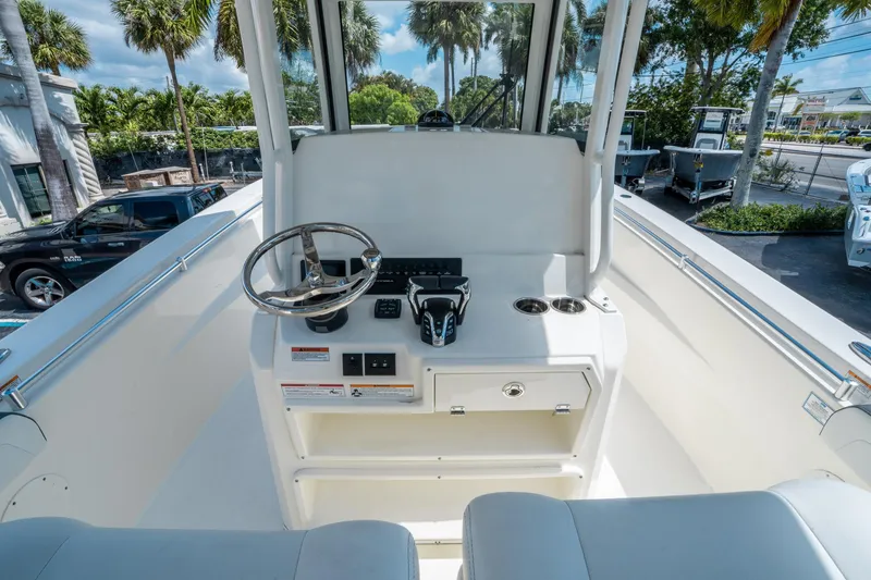 Slide: The Image of 2025 Cobia 285 CC boat helm with steering wheel and controls, surrounded by palm trees. - 19