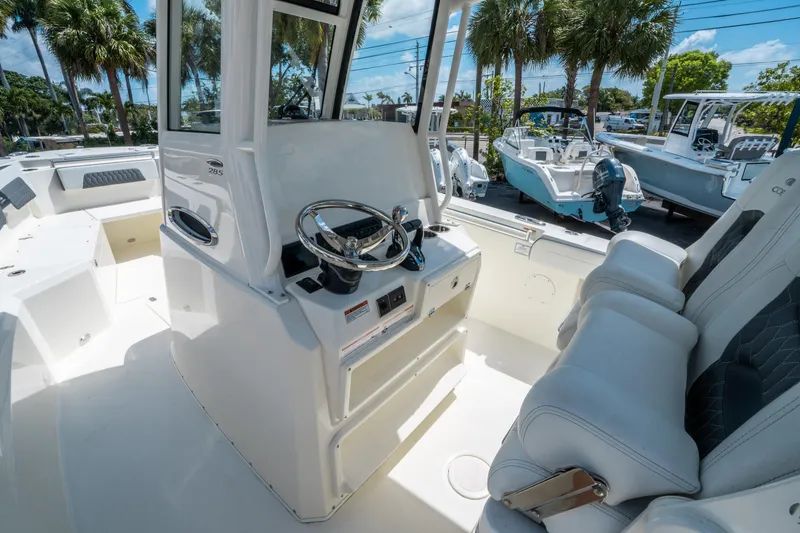 Slide: The Image of 2025 Cobia 285 CC boat interior with steering wheel and seating, under sunny skies. - 20