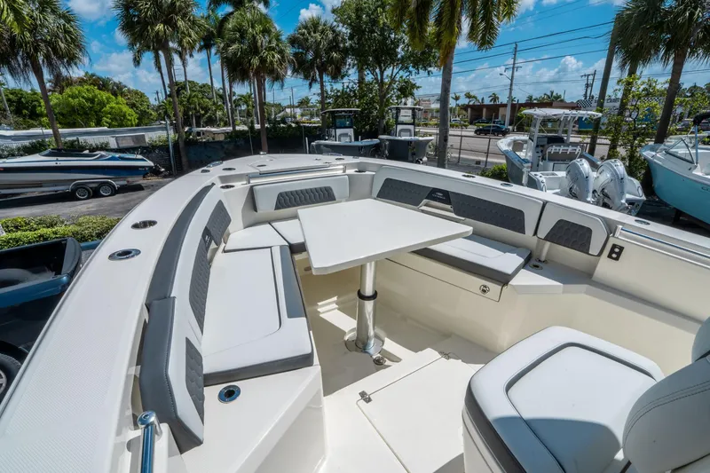 Slide: The Image of 2025 Cobia 285 CC boat interior with seating and table, surrounded by palm trees. - 30