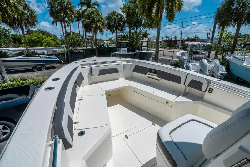 Slide: The Image of 2025 Cobia 285 CC boat interior with seating, surrounded by palm trees and other boats. - 32