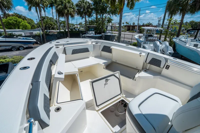 Slide: The Image of 2025 Cobia 285 CC boat interior with open storage compartments and seating under palm trees. - 33
