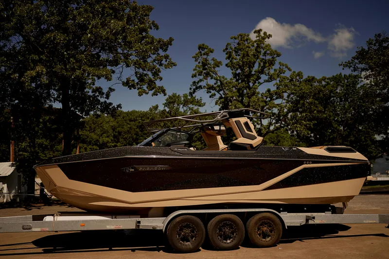 Slide: The Image of 2025 Nautique Super Air Nautique G25 Paragon boat on trailer, surrounded by trees. - 2
