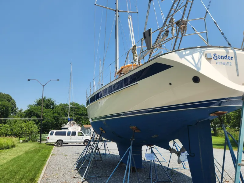 Slide: The Image of 2003 Hallberg-Rassy 46 sailboat on stands, clear sky, parked van nearby. - 5