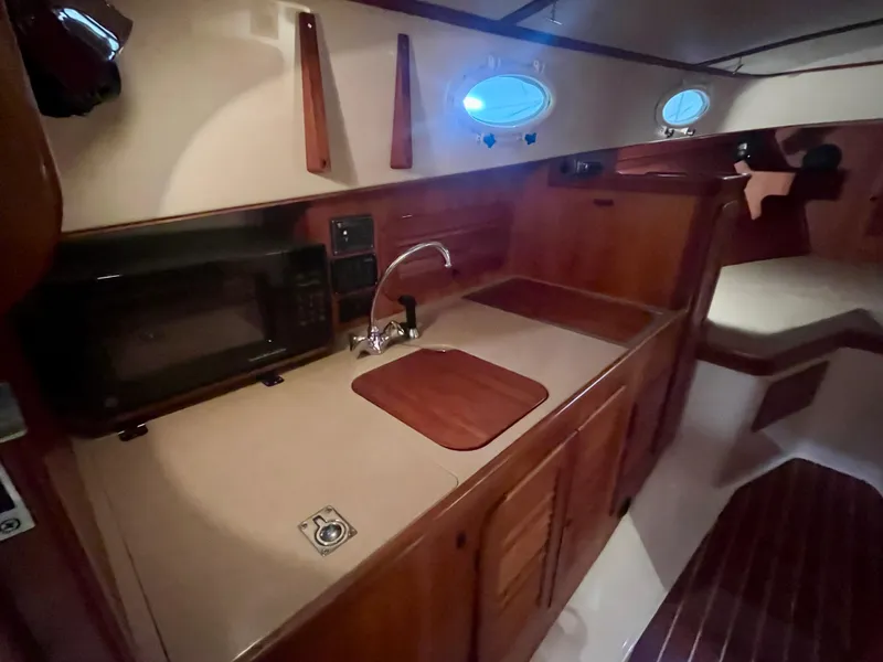 Slide: The Image of 2005 Hinckley Picnic Boat EP interior with kitchenette, featuring wood cabinetry and porthole windows. - 17