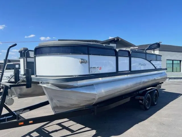 Slide: The Image of 2021 Manitou 23 Aurora LE VP pontoon boat on trailer, parked outdoors under clear blue sky. - 2