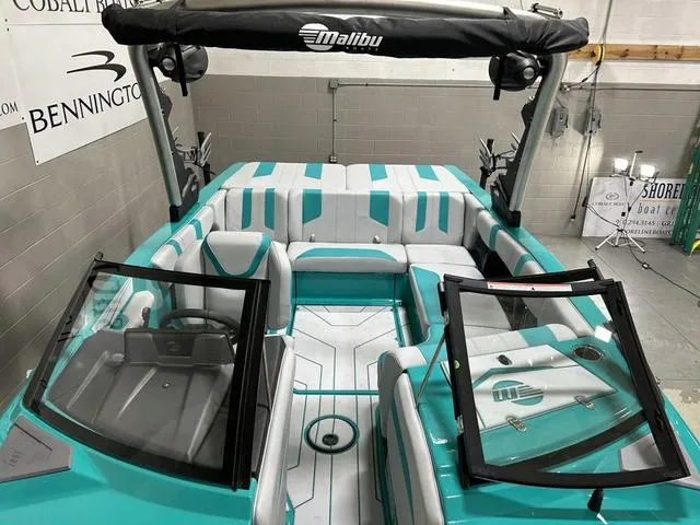 Slide: The Image of 2023 Malibu 21 LX boat interior with teal and white seating, open windshield, and black canopy. - 23