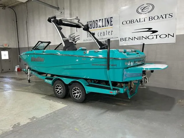 Slide: The Image of 2023 Malibu 21 LX boat in turquoise on a trailer, displayed indoors. - 7