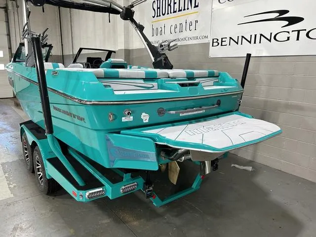 Slide: The Image of 2023 Malibu 21 LX boat in turquoise, displayed indoors at Shoreline Boat Center. - 8