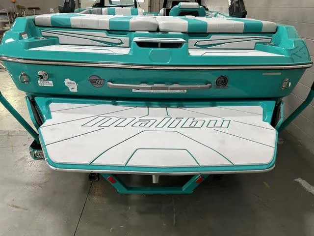 Slide: The Image of 2023 Malibu 21 LX boat, teal and white design, rear view in a showroom. - 9