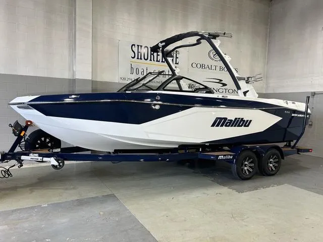 Slide: The Image of 2024 Malibu 23 LSV boat in showroom, blue and white design, on a trailer. - 2