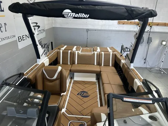Slide: The Image of 2024 Malibu 23 LSV boat interior with tan seating and black accents in showroom. - 29