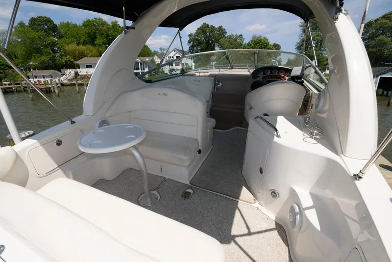 Slide: The Image of 2005 Sea Ray 280 Sundancer boat interior with seating and table, docked by a scenic waterfront. - 2